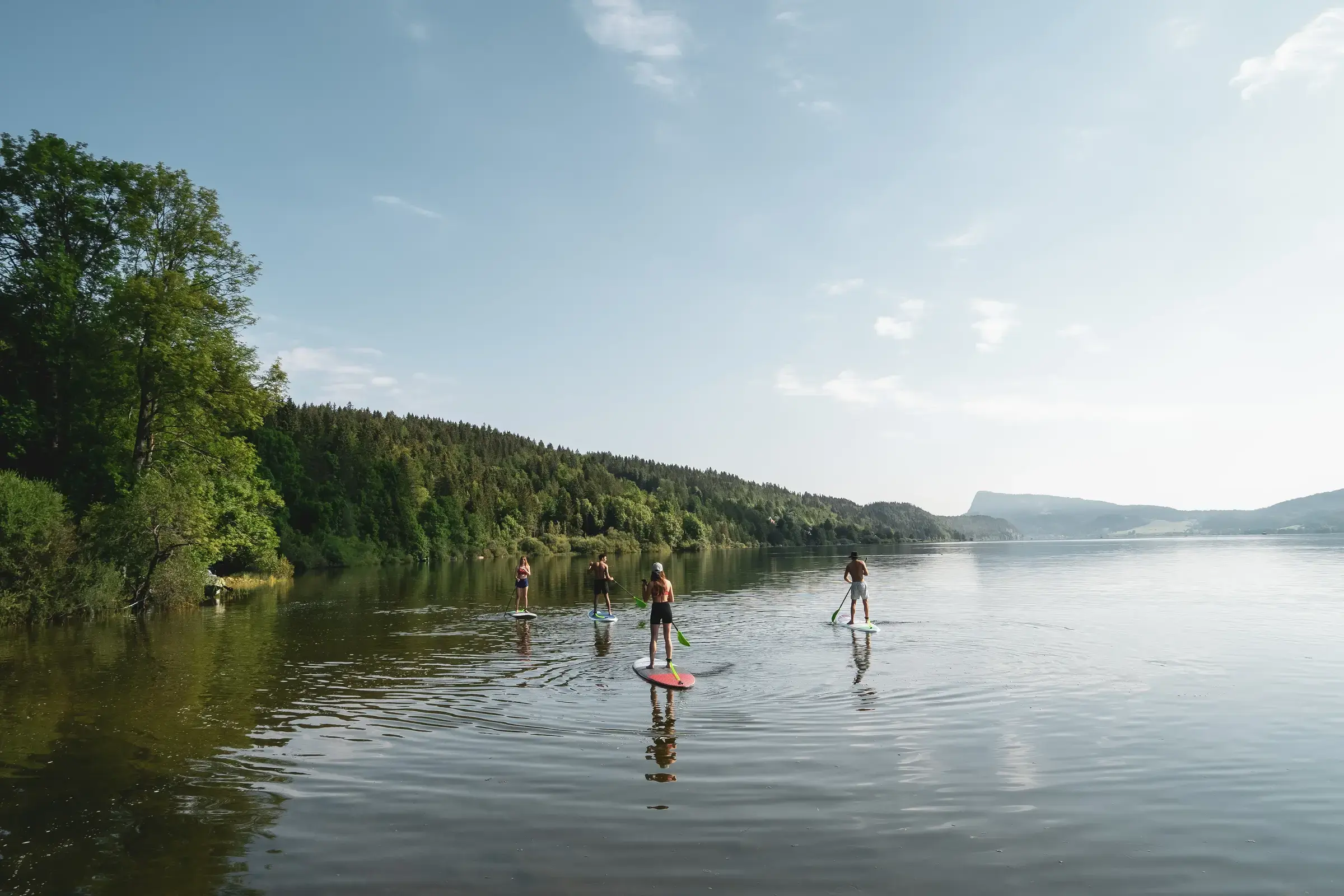 Groupe de quatre personnes en paddle sur le Lac de Joux, entourées par les collines boisées de la Vallée de Joux.